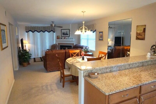 kitchen with ceiling fan with notable chandelier, light carpet, light stone counters, and decorative light fixtures