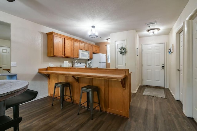 kitchen with white appliances, a kitchen breakfast bar, dark hardwood / wood-style flooring, and kitchen peninsula