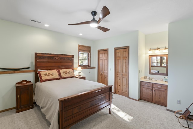 carpeted bedroom with connected bathroom, multiple closets, sink, and ceiling fan