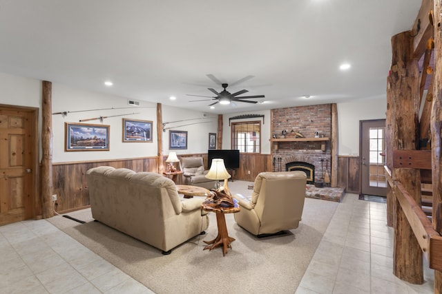 living room featuring ceiling fan, a fireplace, wooden walls, and light carpet