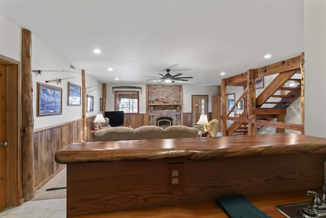 kitchen featuring ceiling fan, a brick fireplace, and wooden walls