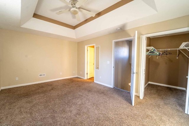 unfurnished bedroom with a closet, carpet floors, ceiling fan, and a tray ceiling