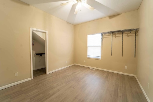 unfurnished bedroom featuring ceiling fan, wood-type flooring, a spacious closet, and a closet