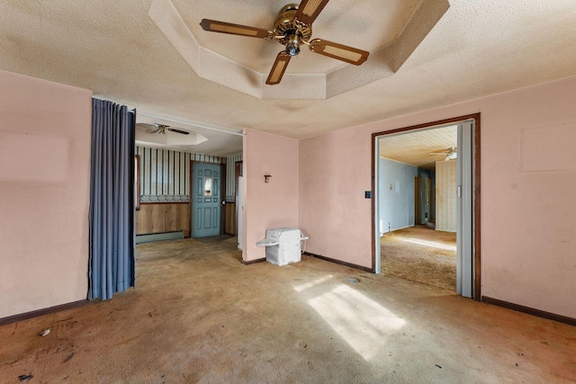 empty room featuring ceiling fan, carpet, baseboard heating, and a tray ceiling