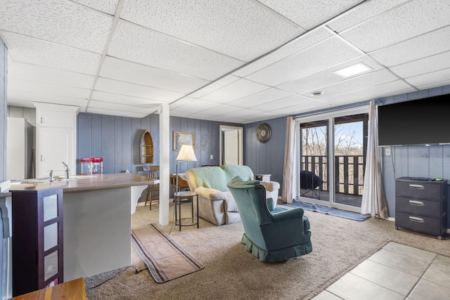 carpeted living room featuring a drop ceiling, sink, and wooden walls