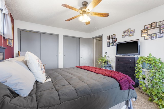 bedroom featuring ceiling fan, a textured ceiling, carpet, and two closets