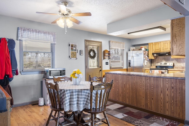 kitchen with a textured ceiling, light hardwood / wood-style flooring, kitchen peninsula, stainless steel appliances, and decorative backsplash