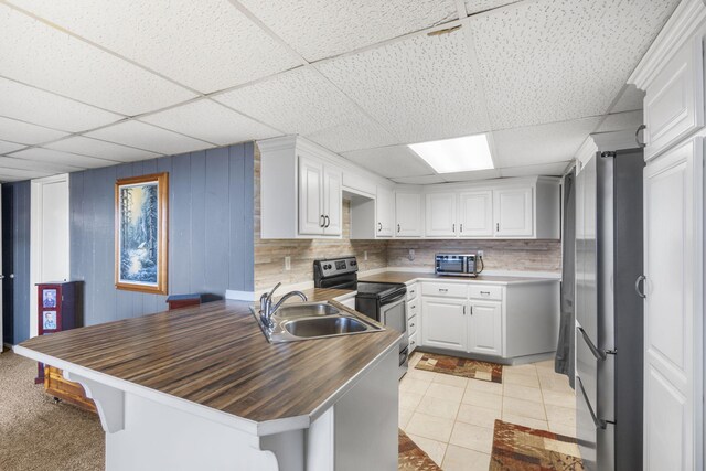 kitchen with sink, a paneled ceiling, kitchen peninsula, stainless steel appliances, and white cabinets