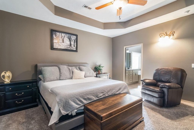 bedroom featuring connected bathroom, a tray ceiling, ceiling fan, and carpet flooring