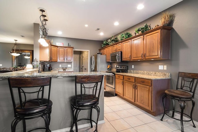 kitchen with appliances with stainless steel finishes, decorative light fixtures, a kitchen bar, and kitchen peninsula