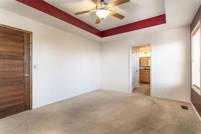 empty room featuring light carpet, ceiling fan, and a tray ceiling