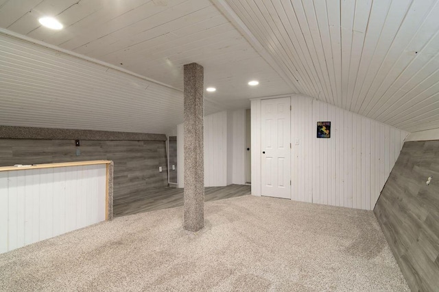 additional living space featuring carpet flooring, vaulted ceiling, and wood walls