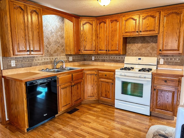 kitchen featuring dishwasher, sink, light wood-type flooring, white range with gas stovetop, and a textured ceiling