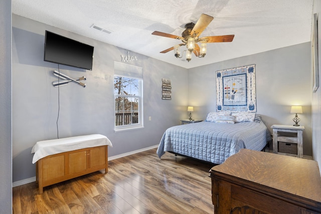 bedroom featuring visible vents, a textured ceiling, baseboards, and wood finished floors