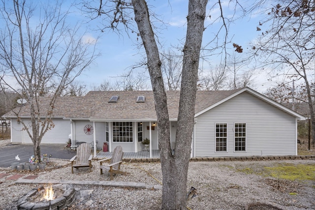 ranch-style home with an attached garage, a fire pit, aphalt driveway, and roof with shingles