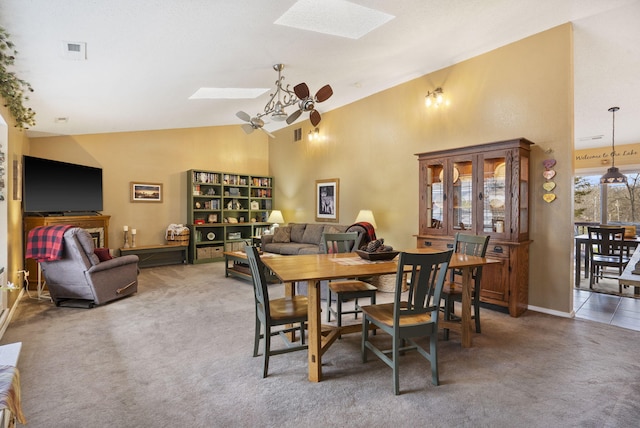 carpeted dining room with ceiling fan, high vaulted ceiling, a skylight, and visible vents