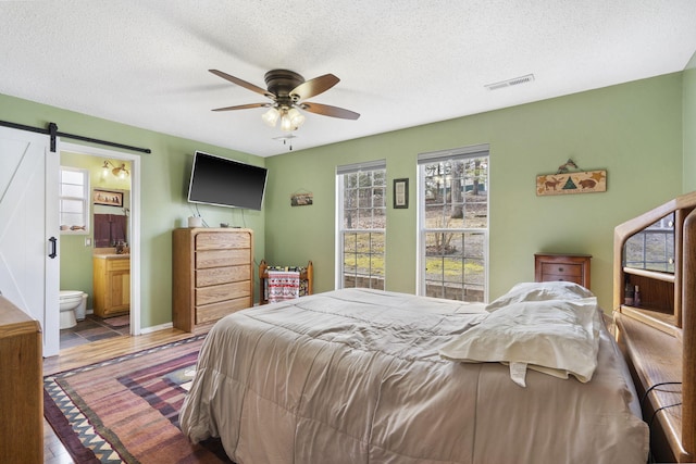 bedroom featuring a barn door, visible vents, connected bathroom, light wood-style flooring, and a textured ceiling