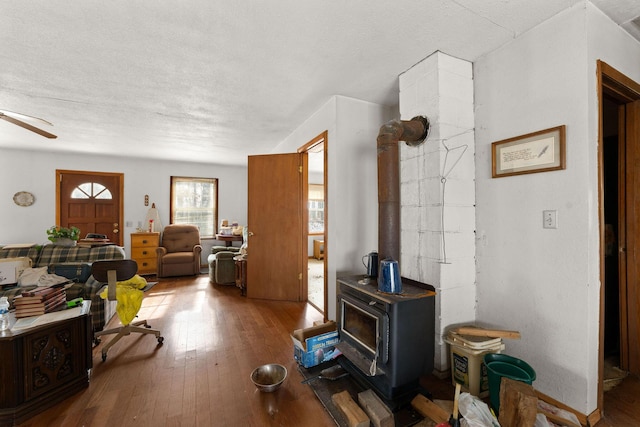 living room with hardwood / wood-style floors, a textured ceiling, ceiling fan, and a wood stove