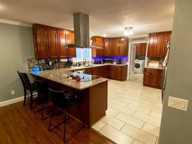 kitchen with sink, a breakfast bar, island range hood, washer / dryer, and kitchen peninsula