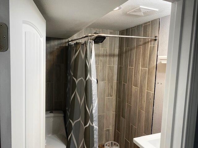 bathroom with toilet, curtained shower, and a textured ceiling