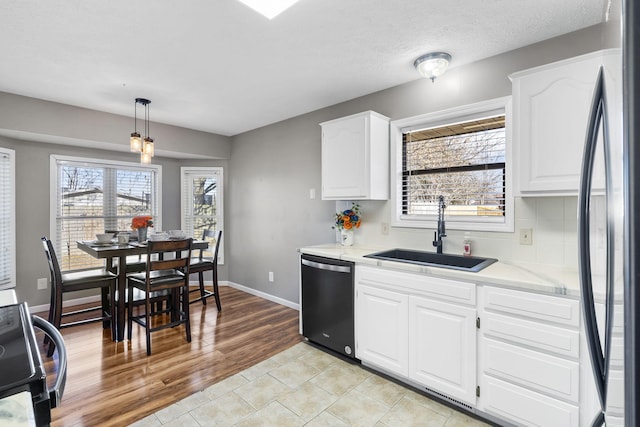 kitchen with black refrigerator, white cabinetry, sink, hanging light fixtures, and stainless steel dishwasher