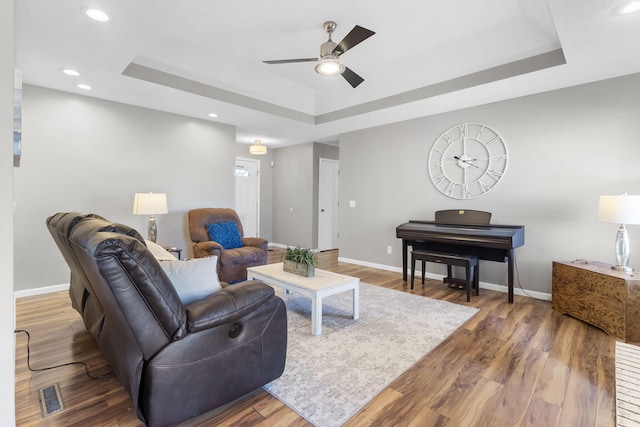 living room with a raised ceiling, dark wood-type flooring, and ceiling fan