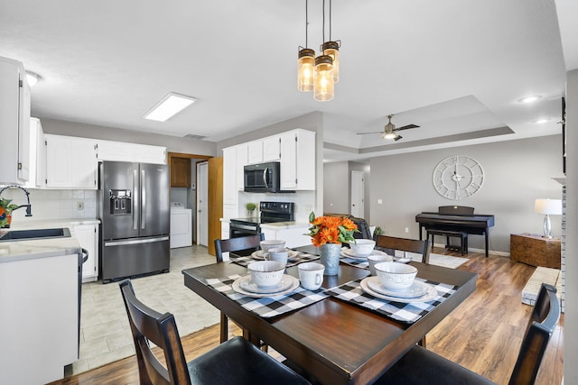 dining area featuring washer / dryer, sink, a tray ceiling, ceiling fan, and light hardwood / wood-style floors