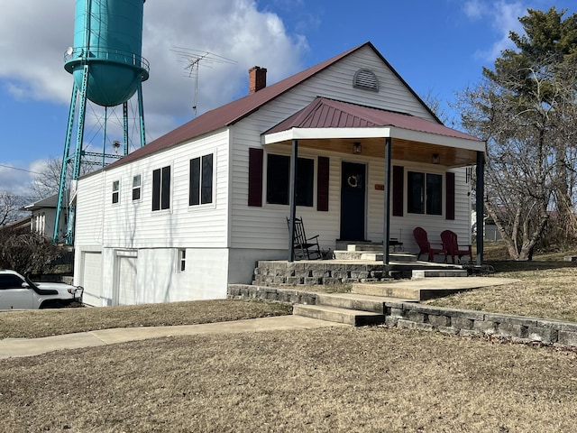 view of front of home featuring metal roof, an attached garage, a porch, and a chimney