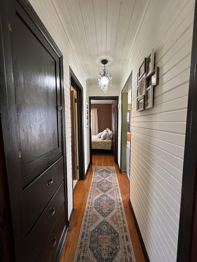 corridor with dark wood-type flooring, wood ceiling, and a chandelier