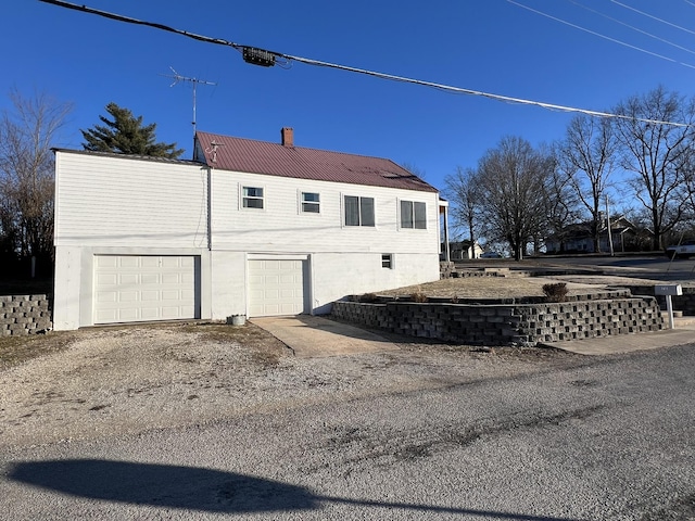 view of side of property featuring a chimney, driveway, and metal roof