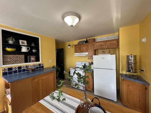 kitchen featuring under cabinet range hood, dark countertops, white appliances, and brown cabinetry