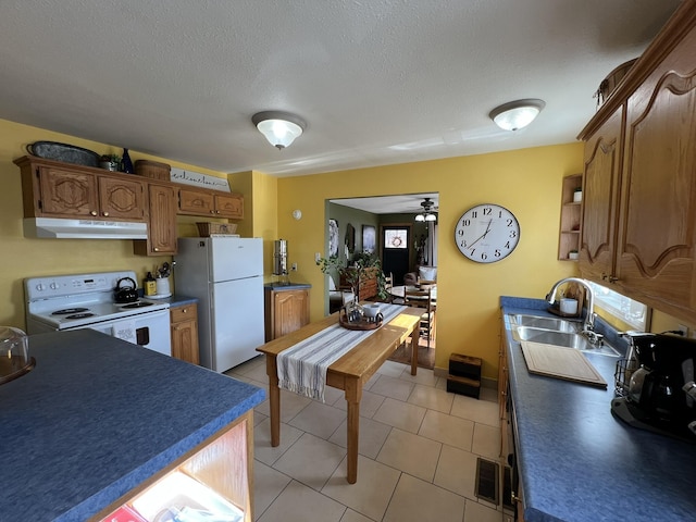 kitchen with white appliances, light tile patterned flooring, a sink, under cabinet range hood, and dark countertops