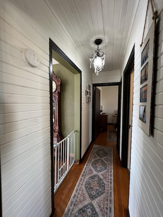 hallway featuring dark wood finished floors, wood ceiling, and an inviting chandelier