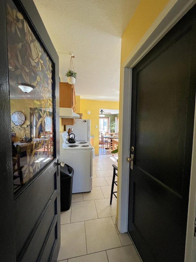 kitchen featuring under cabinet range hood, white appliances, a textured ceiling, and light tile patterned flooring