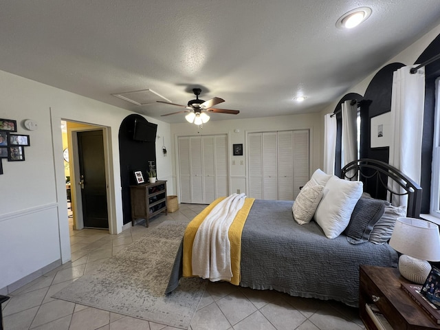 bedroom featuring light tile patterned floors, two closets, a ceiling fan, and a textured ceiling