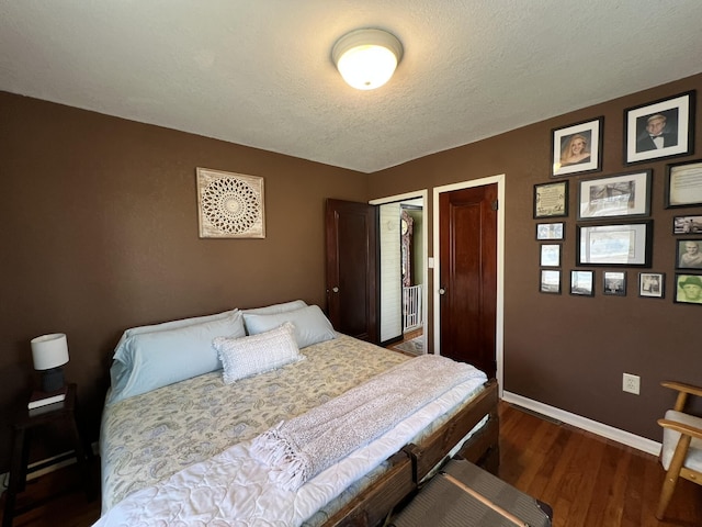 bedroom featuring a textured ceiling, wood finished floors, baseboards, and multiple closets