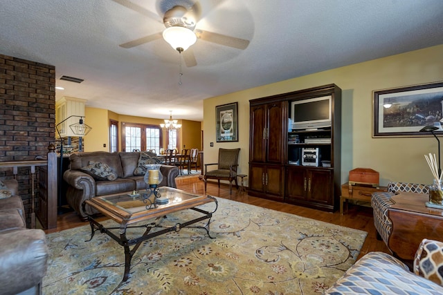 living room featuring hardwood / wood-style flooring, ceiling fan with notable chandelier, and a textured ceiling