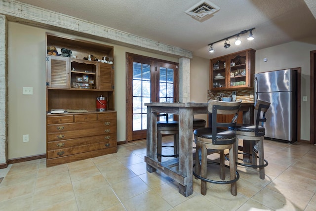 kitchen with stainless steel refrigerator, rail lighting, a textured ceiling, and light tile patterned floors