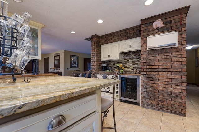 kitchen with a breakfast bar area, light stone counters, light tile patterned floors, beverage cooler, and white cabinets