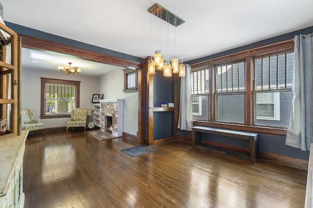 unfurnished dining area featuring an inviting chandelier, dark hardwood / wood-style floors, and a brick fireplace