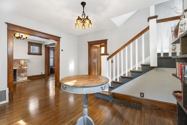 foyer with dark hardwood / wood-style floors, a chandelier, and a brick fireplace