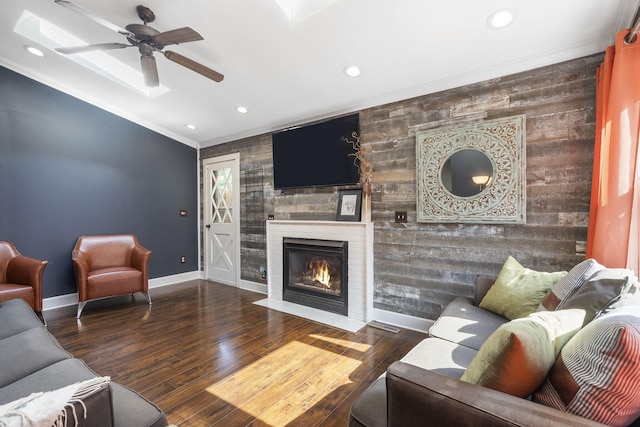 living room with crown molding, dark wood-type flooring, ceiling fan, wooden walls, and a fireplace