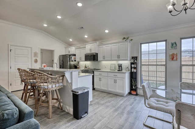 kitchen featuring white cabinetry, appliances with stainless steel finishes, vaulted ceiling, and a kitchen island with sink