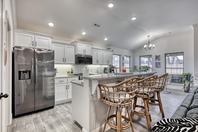 kitchen with tasteful backsplash, stainless steel refrigerator with ice dispenser, a center island with sink, and white cabinets