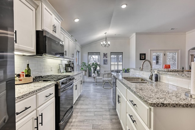 kitchen featuring vaulted ceiling, black gas range oven, white cabinetry, sink, and a kitchen island with sink