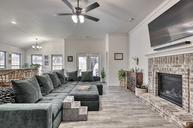 living room with crown molding, light hardwood / wood-style floors, a brick fireplace, ceiling fan with notable chandelier, and vaulted ceiling