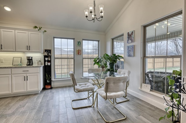 dining room featuring vaulted ceiling, ornamental molding, light wood-type flooring, and an inviting chandelier