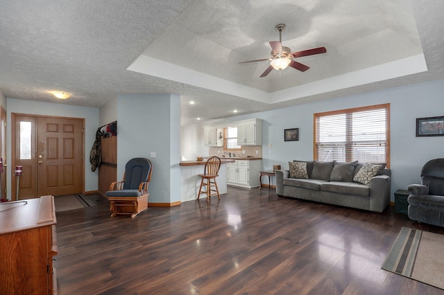 living room with dark wood-type flooring, ceiling fan, and a tray ceiling