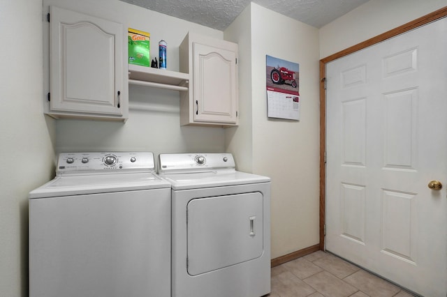 clothes washing area with cabinets, washer and clothes dryer, a textured ceiling, and light tile patterned floors