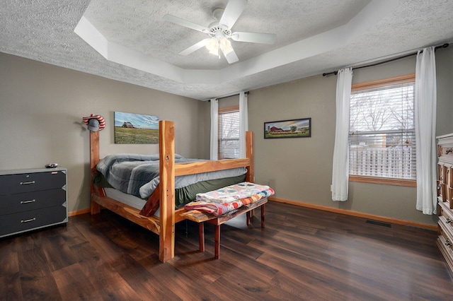 bedroom with dark hardwood / wood-style floors, a textured ceiling, a raised ceiling, and ceiling fan